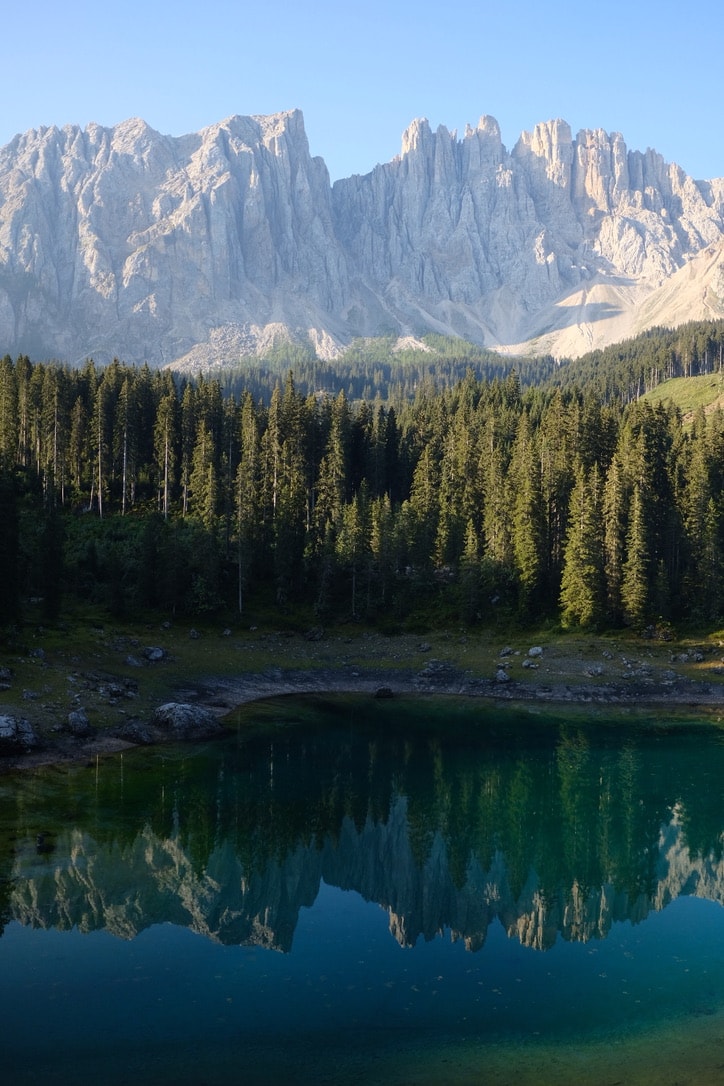 The turquoise water of Lago di Carezza reflecting a dense spruce forest, with the pale Latemar ridge rising behind