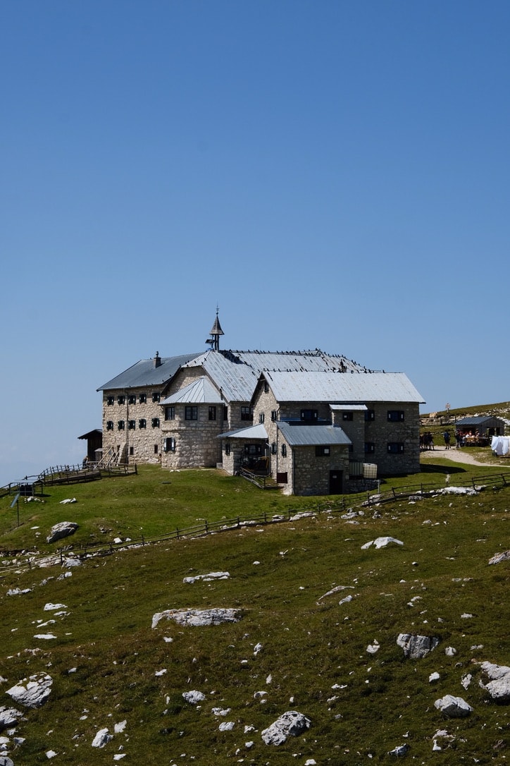 The stone Schlernhaus hut with its small bell tower, standing on a rocky grass plateau under a deep blue sky