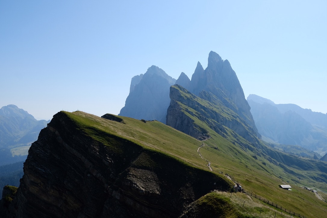 The tilted grass ridge of Seceda falling away to the left, with the Fermeda towers rising behind it and a hut on the slope to the right